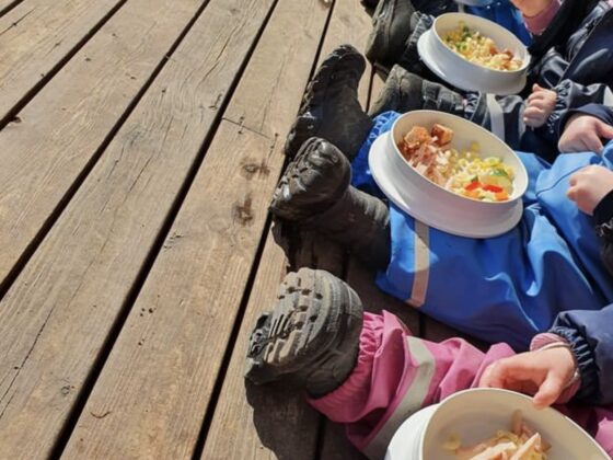 Barn på rad med mattallrik i famnen. Vårsol ute och barnen äter lunch på altanen. Vemdalens förskola.